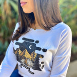 Long-sleeved pullover. Graphic includes mountains, evergreen trees, moon and stars, and a bear with flowers in her hair.