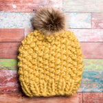 A generous faux fur pom-pom looks like real fur, on a colorful chunky knit hat.