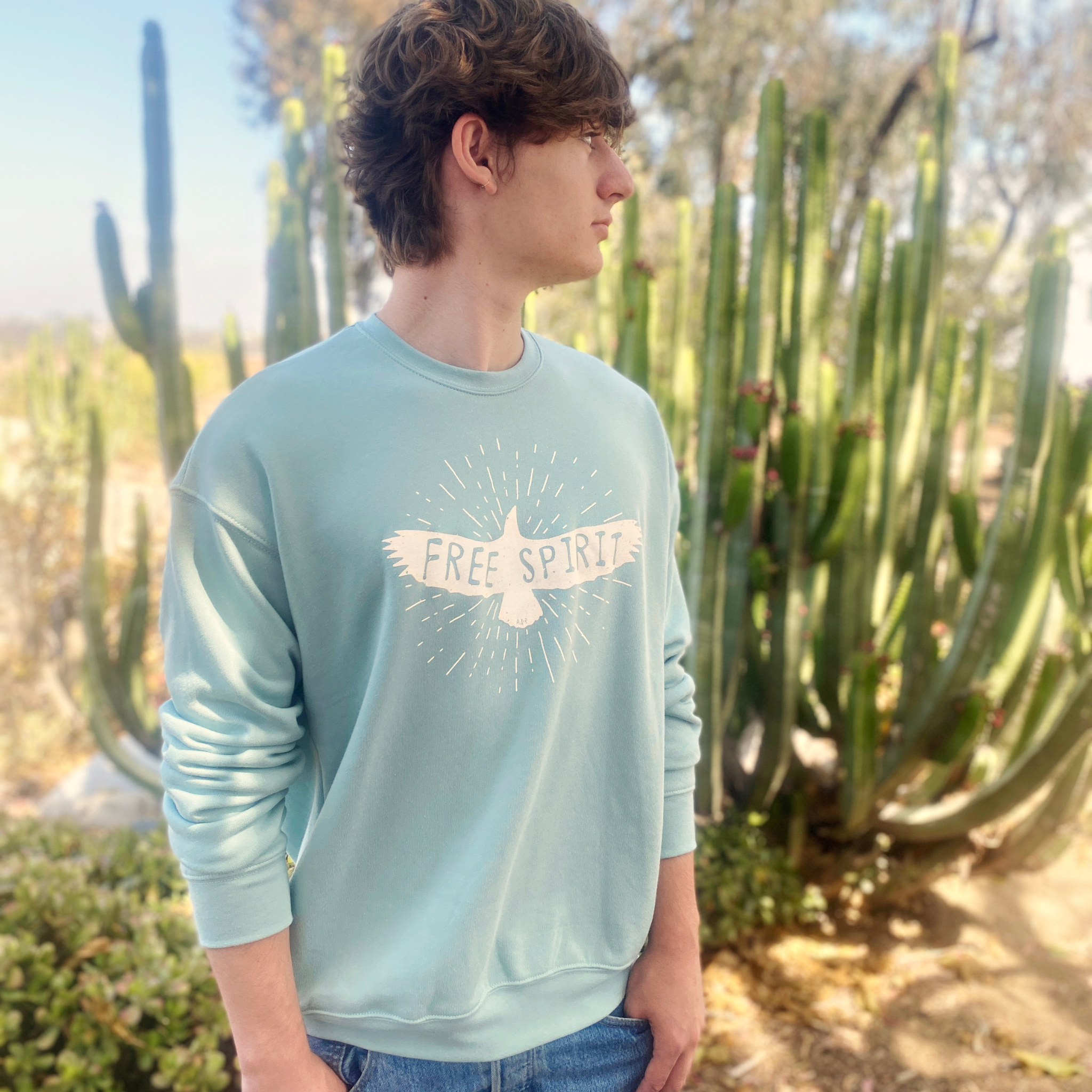 Man with light blue, long-sleeved sweatshirt that has a graphic of a soaring bird with the words "FREE SPIRIT" across its wings.