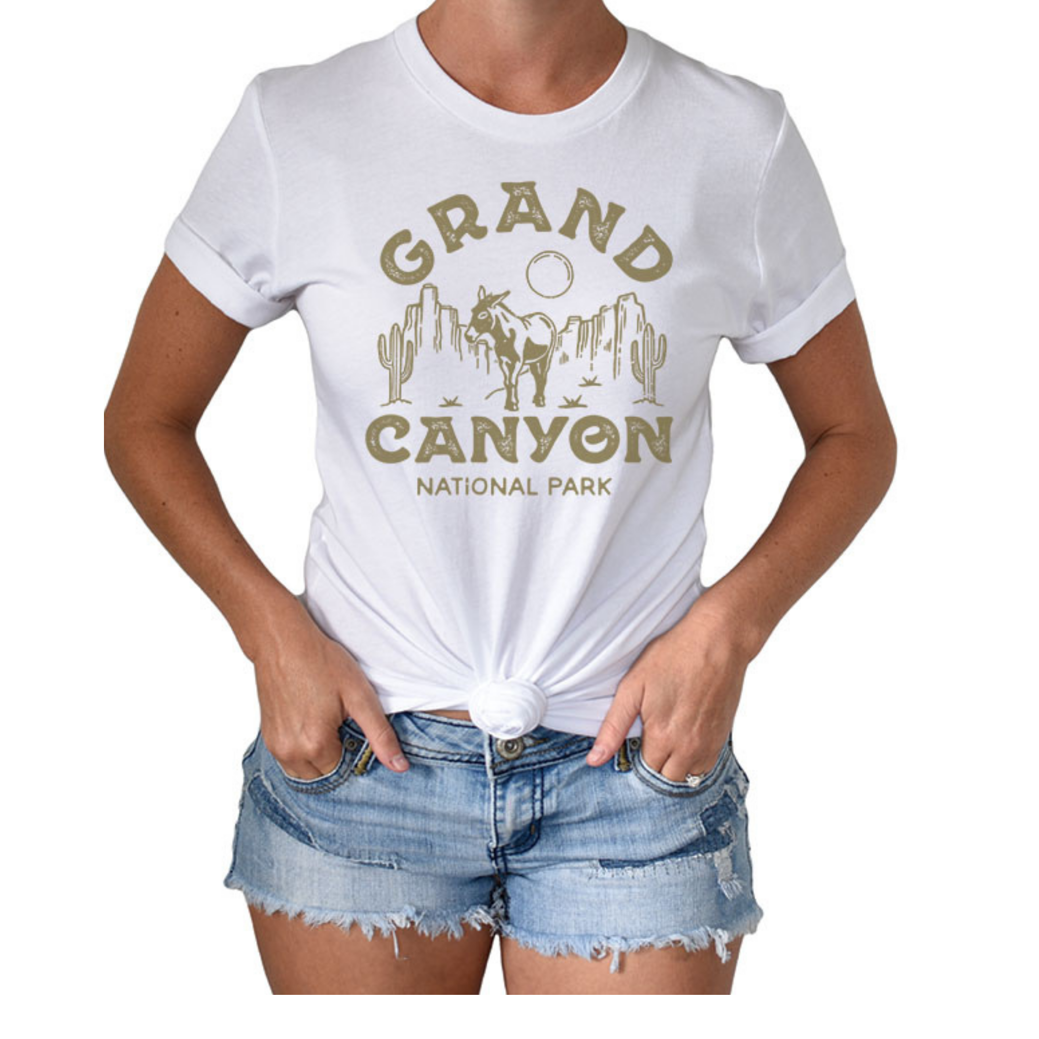 Woman wearing jean shorts and a short sleeved, crew neck t-shirt with a graphic that says "Grand Canyon National Park" around a canyon scene with cacti, a donkey, and a circle sun/moon.