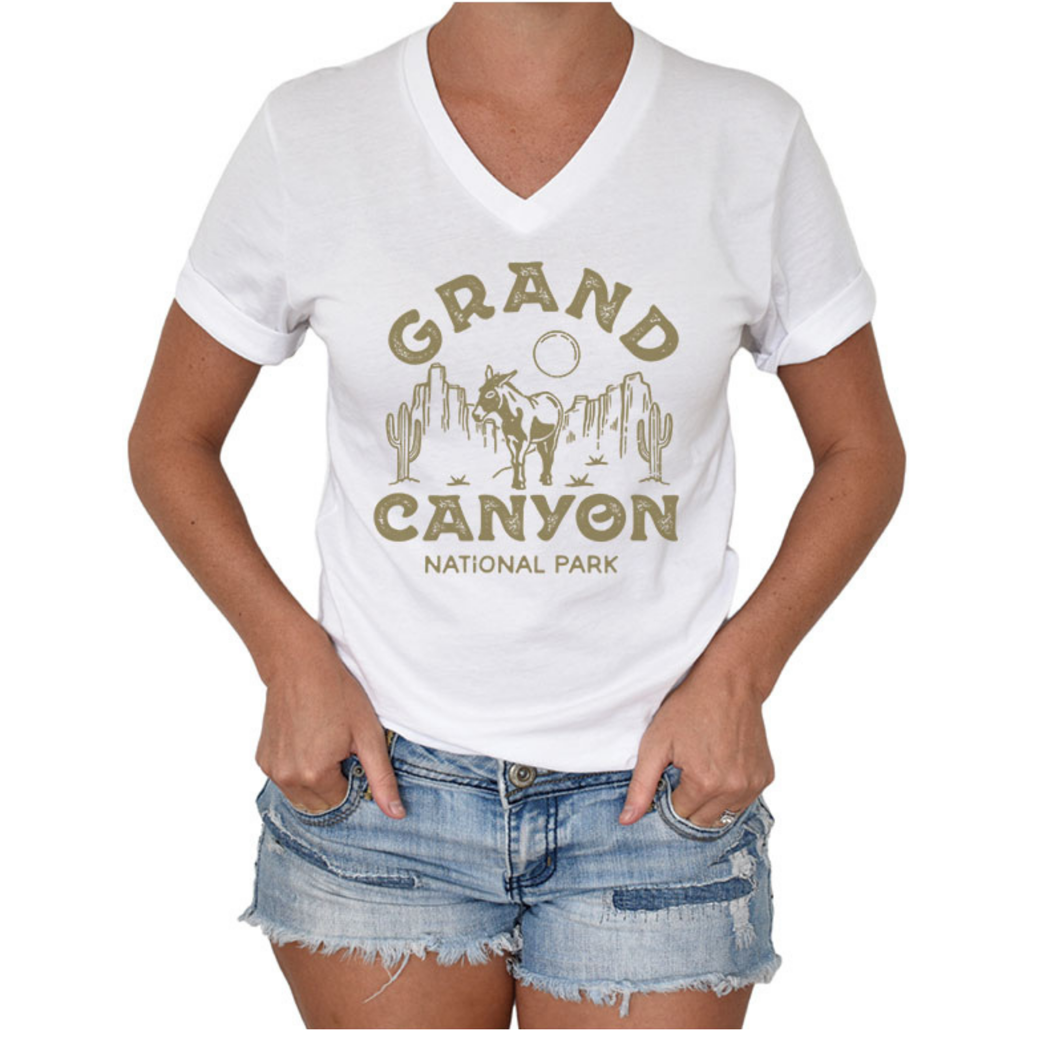 Woman wearing jean shorts and a short sleeved, v-neck t-shirt with a graphic that says "Grand Canyon National Park" around a canyon scene with cacti, a donkey, and a circle sun/moon.