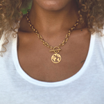 Close up of woman in white shirt with gold chain necklace and world map pendant charm.